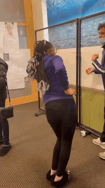 a woman in a purple sweatshirt and black pants is standing in front of a white board