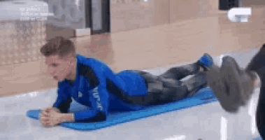 a man in a blue shirt is laying on a blue mat on the floor .