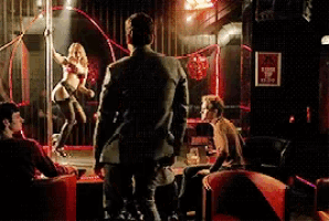 a man in a suit is watching a pole dancer in a club