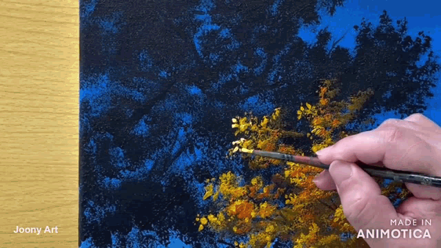 a person is painting a tree with yellow leaves on a wooden table