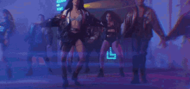 a group of people are dancing in a dark room with a neon sign in the background .