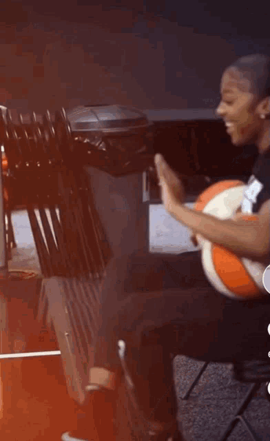 a woman is sitting on a chair holding a basketball and giving a high five .