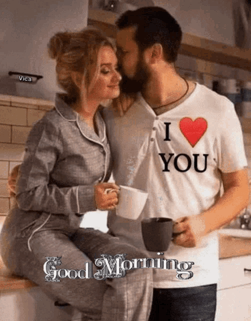 a man is kissing a woman on the cheek while holding a cup of coffee in a kitchen .