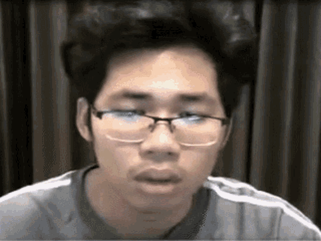 a man wearing glasses and a grey shirt is looking at the camera .