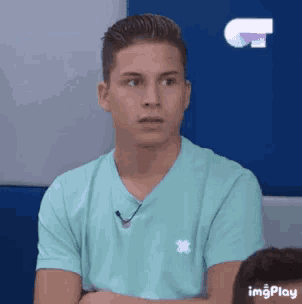 a man in a blue shirt is sitting with his arms crossed and looking at the camera .