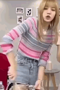 a woman in a pink and blue striped sweater and blue shorts is standing in front of a table .
