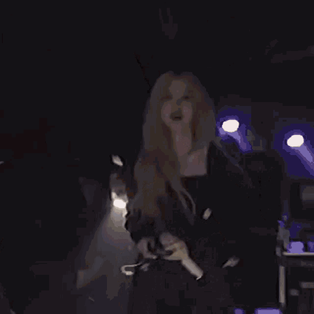 a woman is singing into a microphone on a stage while a man looks on .
