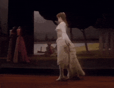 a woman in a pink and white dress stands with her arms outstretched