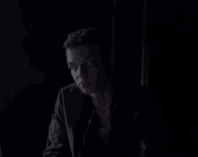 a man with a ponytail is sitting in the dark looking at something .