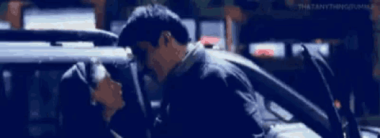 a man and a woman are kissing in a car in the rain .