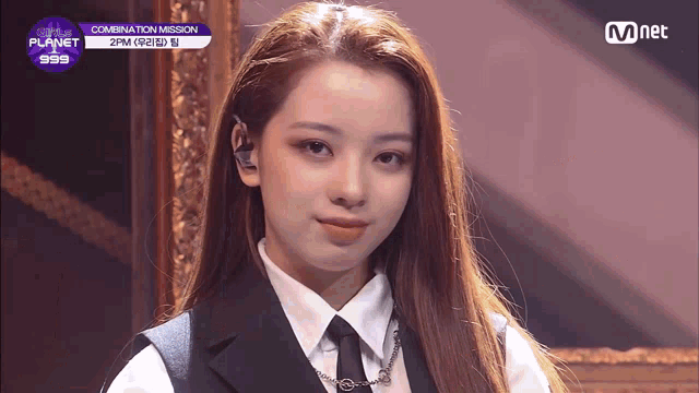 a girl in a suit and tie is standing in front of a mnet banner