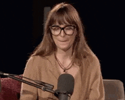 a woman wearing glasses is sitting in front of a microphone and smiling .