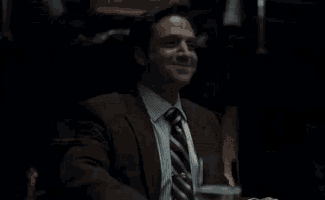 a man in a suit and tie is sitting at a table with a glass of wine in his hand .