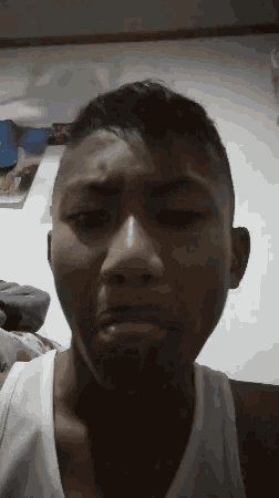 a young man in a white tank top makes a funny face