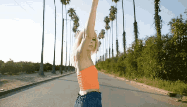 a woman in an orange top is standing on a road