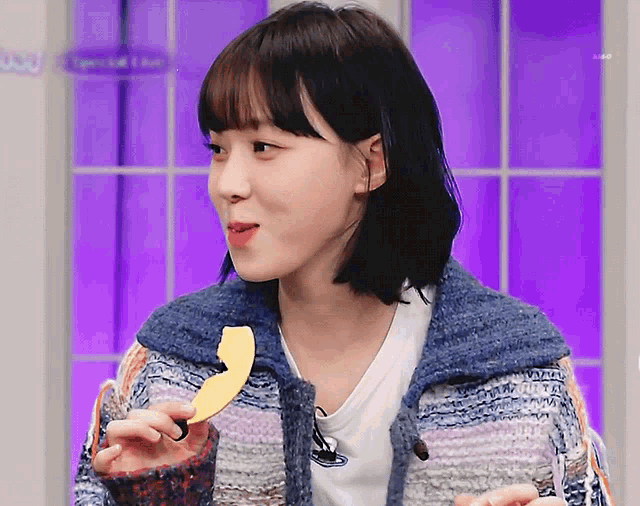 a woman in a blue sweater is eating a piece of fruit