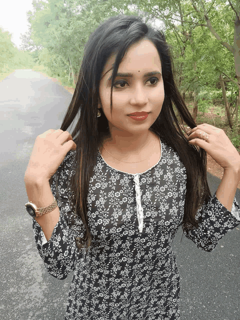 a woman in a black and white floral dress is standing on a road