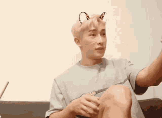 a young man wearing cat ears is sitting on a couch taking a picture of himself .