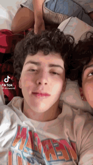 a boy with curly hair is laying on a bed next to a girl .