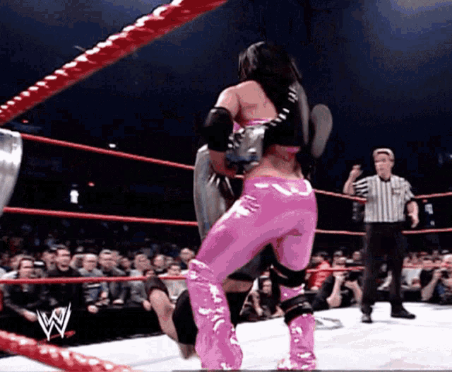 a woman in pink pants is wrestling a man in a wrestling ring with a w on the ropes