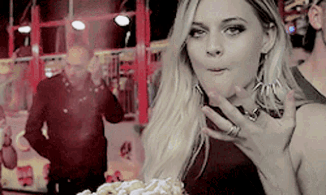 a woman with a ring on her finger is eating a cone with powdered sugar at a carnival .