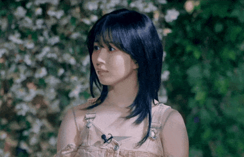 a woman with blue hair and overalls is standing in front of flowers .