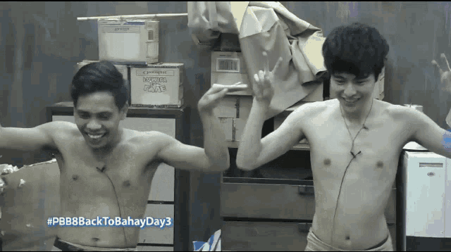 two shirtless men are dancing in front of a stack of boxes one of which says moving house on it