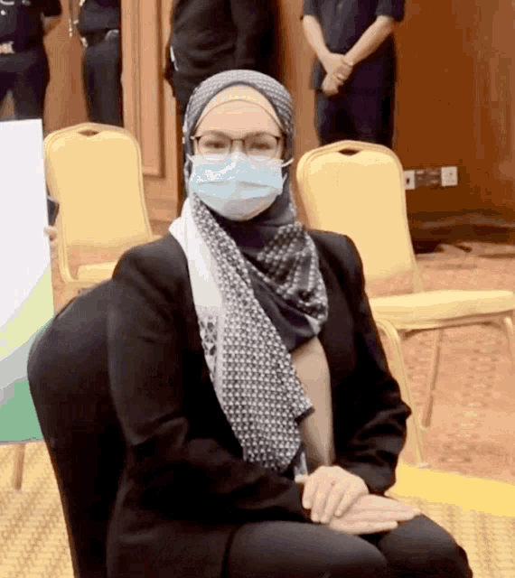 a woman wearing glasses and a mask sits in a chair