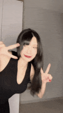 a young woman in a black dress is giving a peace sign .