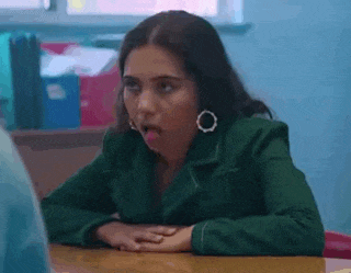 a woman in a green jacket is sticking her tongue out while sitting at a desk .