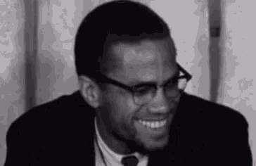 a black and white photo of a man wearing glasses and a suit and tie .