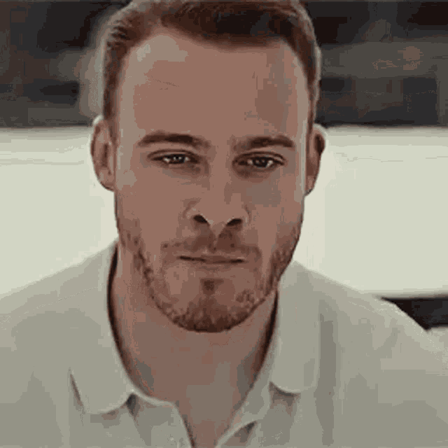a close up of a man with a beard wearing a white shirt and looking at the camera .
