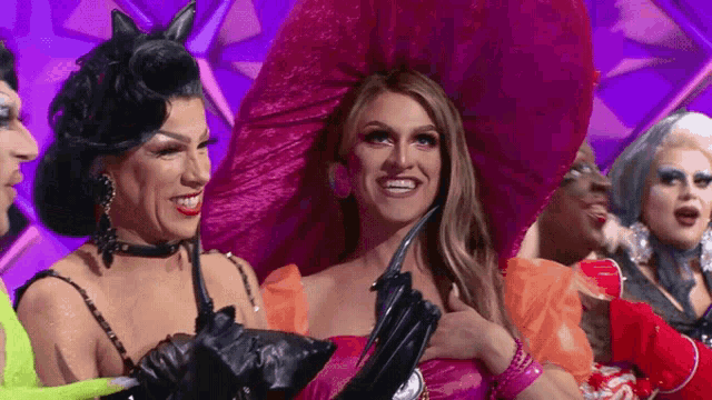 a group of drag queens are posing for a picture and smiling .