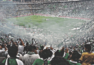 a crowd of people watching a soccer game with smoke coming out of the stands