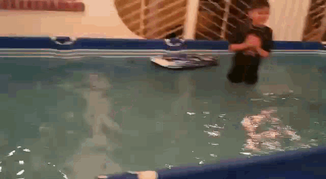 a young boy is jumping into a pool with a toy boat