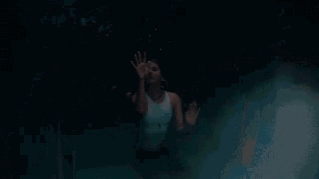 a woman in a white tank top is swimming underwater in a pool with fish .