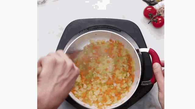 a person is stirring carrots , celery , and onions in a pan .