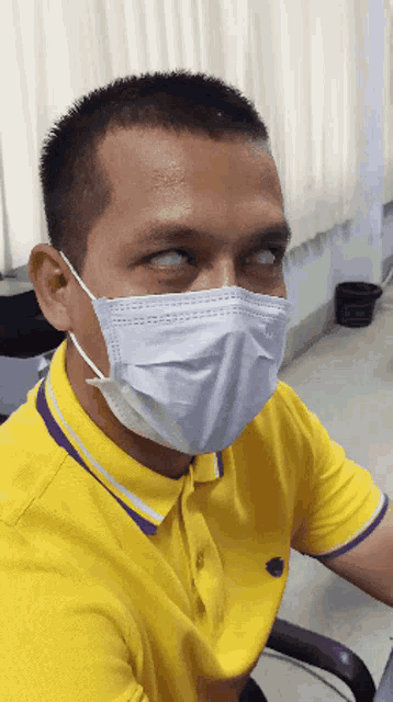 a man wearing a yellow shirt and a mask looks at the camera