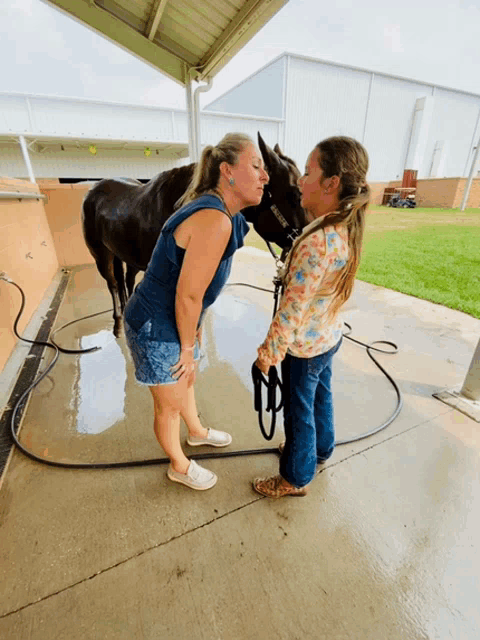 a woman kisses a horse on the nose while a little girl holds the reins