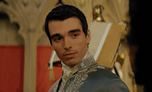 a man in a blue coat with gold embroidery is looking at something