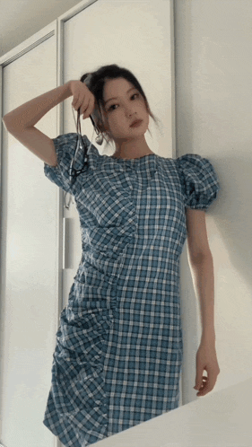 a woman in a blue plaid dress is standing in front of a white cabinet