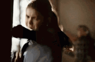 a woman is standing in front of a window in a dark room and looking out the window .