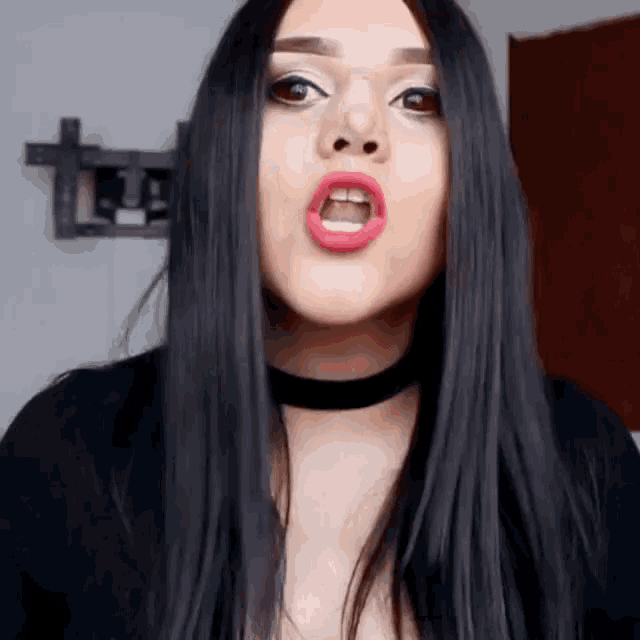 a woman with long black hair is wearing a black choker and red lipstick