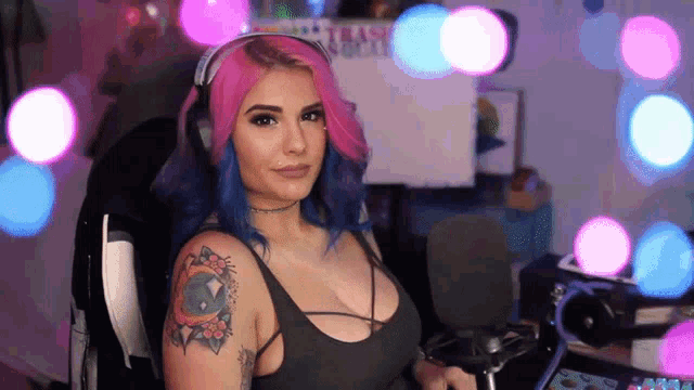 a woman with pink and blue hair is wearing headphones and sitting in front of a microphone