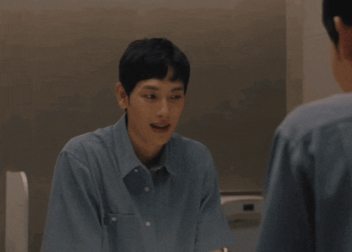 a man in a blue shirt looks at himself in the mirror