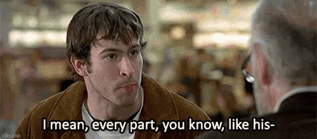 a man in a brown jacket is talking to another man .