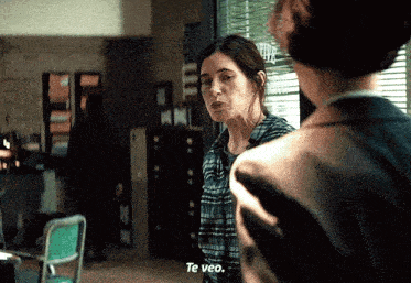 a woman in a plaid shirt is talking to a man in a room and says te veo