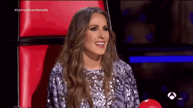 a woman is sitting in a red chair on a television show and smiling .