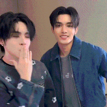 two young men are standing next to each other in a room . one of the men is covering his mouth with his hand .