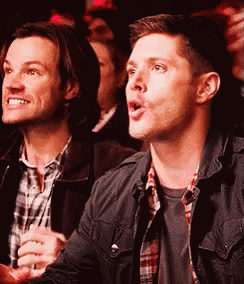 two men are sitting in a crowd watching a show and one of them is making a funny face .
